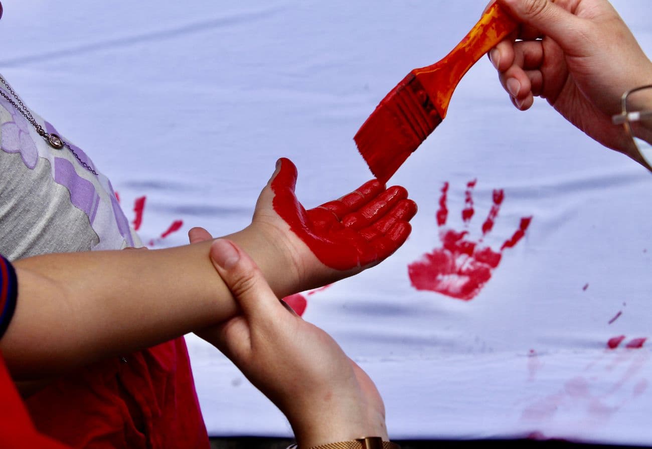 Niños pintando sus manos rojas en el mural blanco de paz
